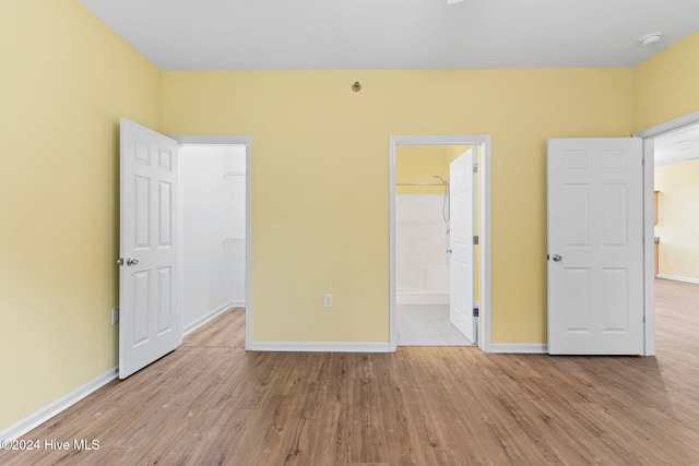 unfurnished bedroom featuring a walk in closet, light hardwood / wood-style flooring, ensuite bath, and a closet