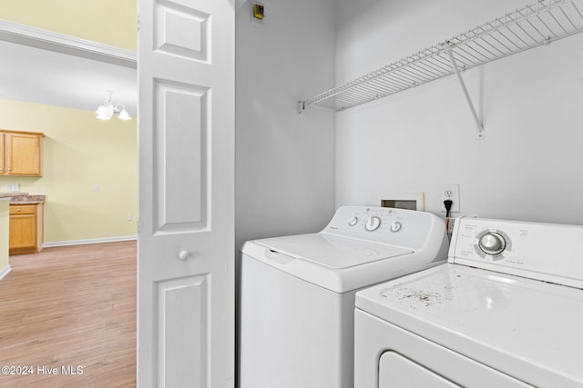 laundry area with an inviting chandelier, washer and clothes dryer, and light hardwood / wood-style flooring