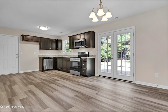 kitchen with hanging light fixtures, appliances with stainless steel finishes, light wood-type flooring, french doors, and sink