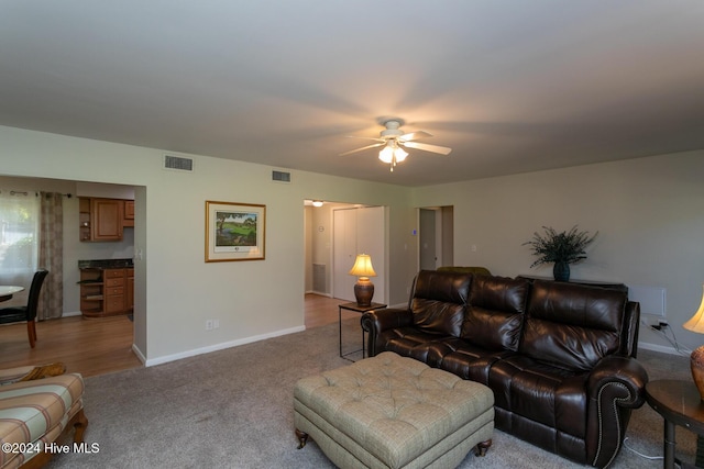 living area featuring light colored carpet, baseboards, a ceiling fan, and visible vents