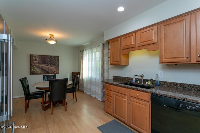 kitchen with a sink, black dishwasher, brown cabinets, dark stone counters, and light wood finished floors