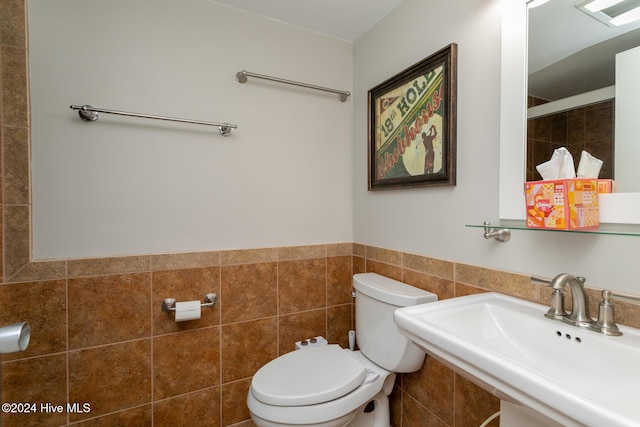 bathroom with a sink, tile walls, toilet, a wainscoted wall, and tiled shower