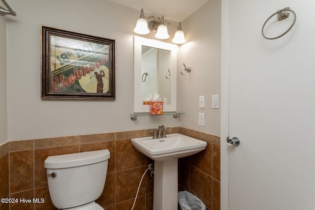 bathroom with tile walls, toilet, a wainscoted wall, and a sink