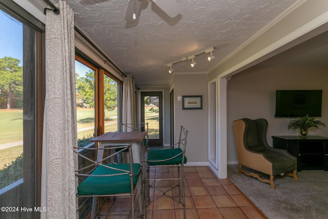 sunroom featuring a textured ceiling, track lighting, tile patterned floors, crown molding, and baseboards