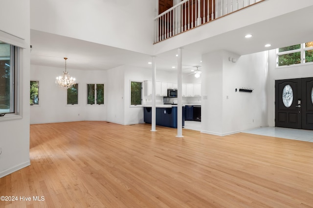 unfurnished living room featuring ceiling fan with notable chandelier, light hardwood / wood-style flooring, and a high ceiling