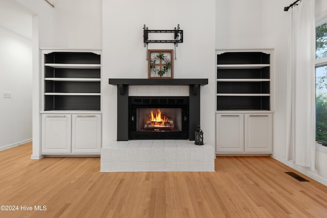 unfurnished living room featuring a tiled fireplace, built in features, and light hardwood / wood-style floors