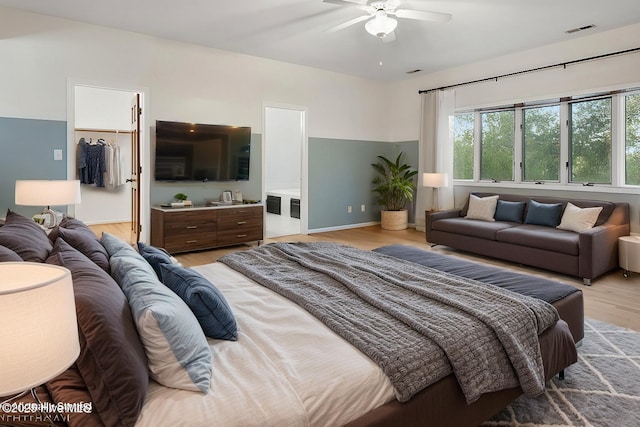 bedroom featuring connected bathroom, a walk in closet, ceiling fan, light hardwood / wood-style floors, and a closet