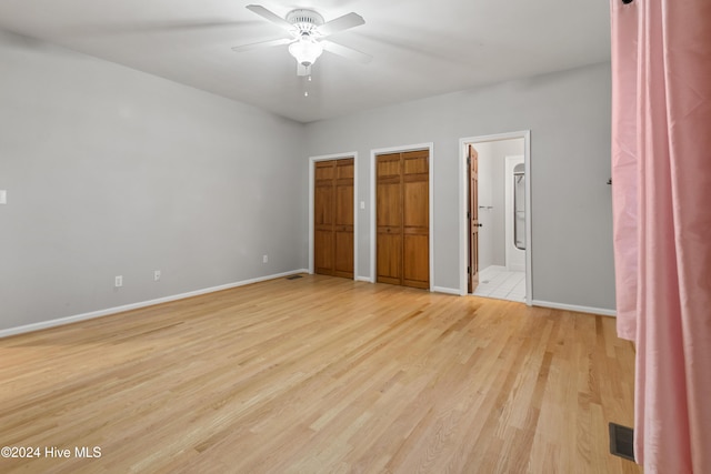 unfurnished bedroom featuring two closets, light wood-type flooring, connected bathroom, and ceiling fan