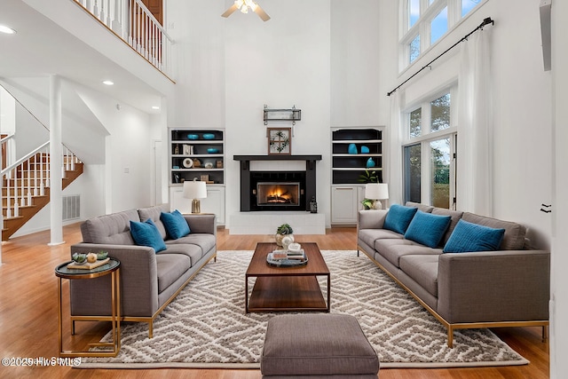 living room featuring hardwood / wood-style flooring, a towering ceiling, a tiled fireplace, and ceiling fan