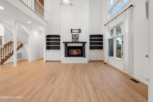 unfurnished living room with a high ceiling, ceiling fan, a fireplace, and light hardwood / wood-style flooring