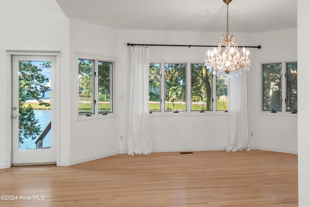 unfurnished dining area featuring a wealth of natural light, light hardwood / wood-style flooring, a chandelier, and a water view