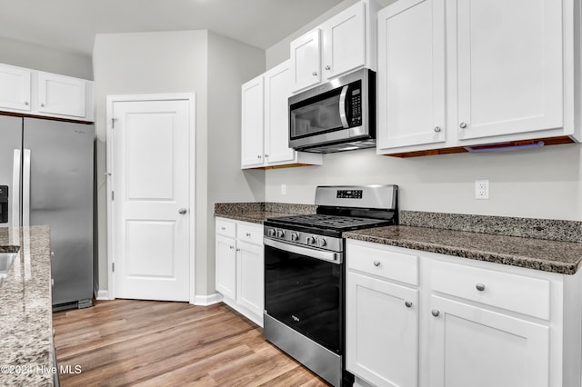 kitchen featuring light hardwood / wood-style floors, white cabinets, stainless steel appliances, and dark stone counters