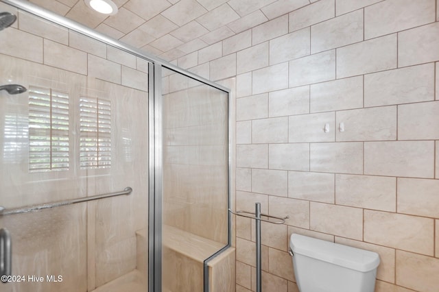 bathroom with tile walls, toilet, and a shower with shower door