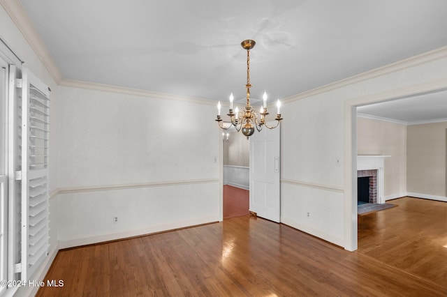 unfurnished dining area featuring dark wood-type flooring, ornamental molding, a notable chandelier, and a brick fireplace