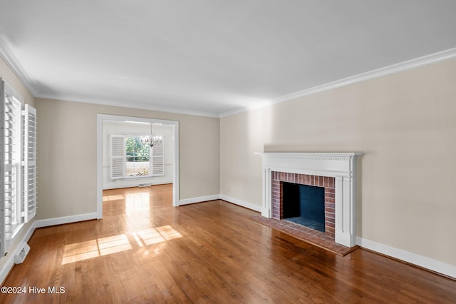 unfurnished living room featuring ornamental molding, hardwood / wood-style floors, a brick fireplace, and an inviting chandelier