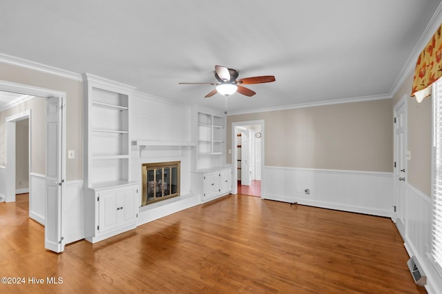 unfurnished living room with hardwood / wood-style flooring, ceiling fan, crown molding, and built in shelves