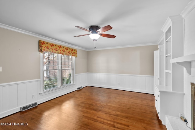 empty room featuring dark wood-type flooring, built in features, ceiling fan, and crown molding