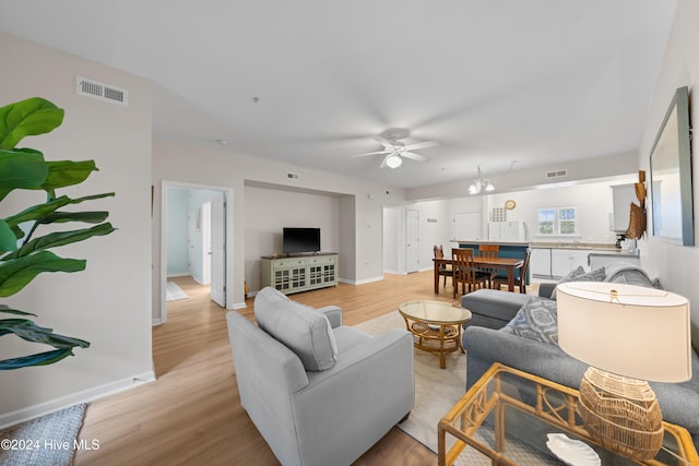 living room featuring ceiling fan with notable chandelier and light hardwood / wood-style floors