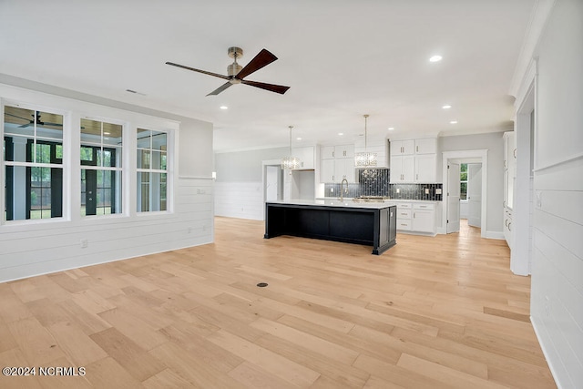 kitchen featuring white cabinets, an island with sink, light hardwood / wood-style flooring, pendant lighting, and crown molding