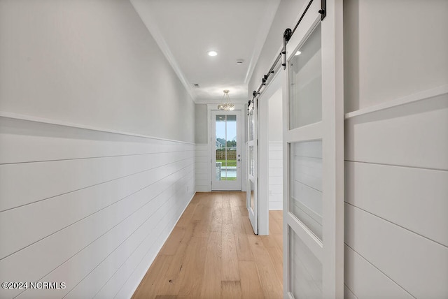 hall featuring crown molding, light wood-type flooring, and a barn door