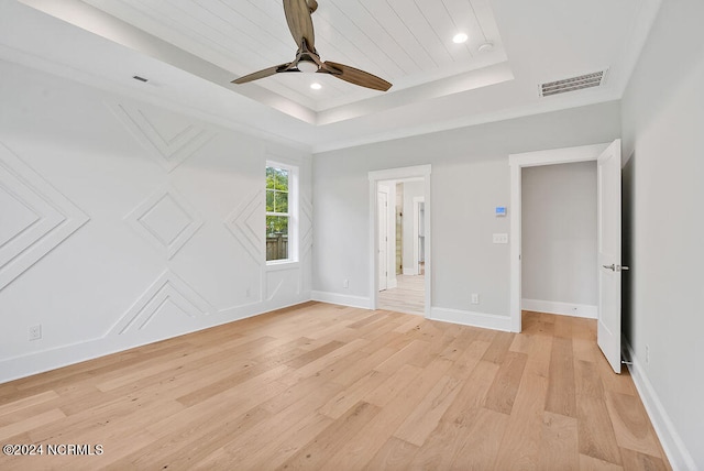 empty room with ceiling fan, light wood-type flooring, and a raised ceiling