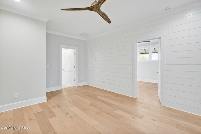 empty room featuring ornamental molding, ceiling fan, light hardwood / wood-style floors, and wood walls