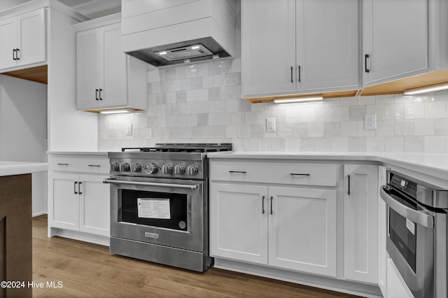 kitchen featuring custom range hood, appliances with stainless steel finishes, tasteful backsplash, dark hardwood / wood-style flooring, and white cabinetry