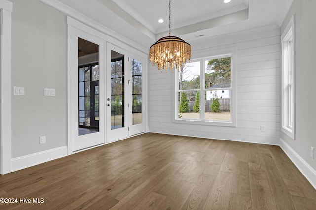 unfurnished dining area featuring hardwood / wood-style flooring, a raised ceiling, a wealth of natural light, and a chandelier