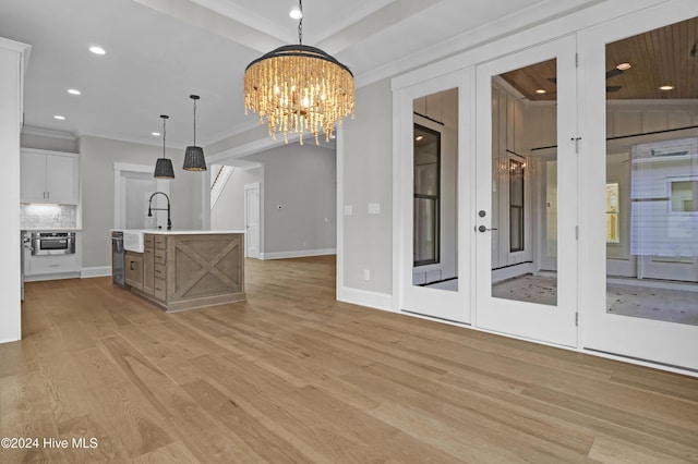 interior space featuring tasteful backsplash, a kitchen island with sink, pendant lighting, a chandelier, and white cabinetry