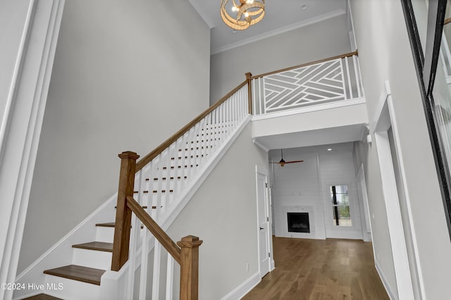 staircase featuring hardwood / wood-style floors, a high ceiling, an inviting chandelier, ornamental molding, and a fireplace