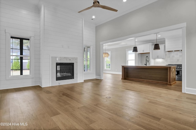 unfurnished living room with a high ceiling, sink, light hardwood / wood-style flooring, ceiling fan, and a fireplace