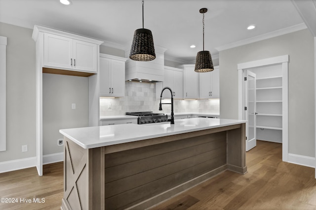 kitchen with pendant lighting, a kitchen island with sink, white cabinets, tasteful backsplash, and light hardwood / wood-style floors