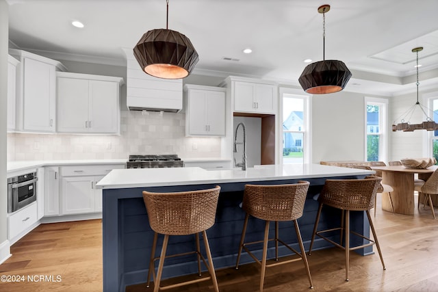 kitchen with light hardwood / wood-style floors, white cabinetry, decorative light fixtures, and an island with sink