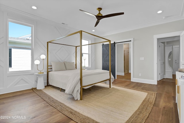 bedroom with ceiling fan, crown molding, wood-type flooring, and a barn door