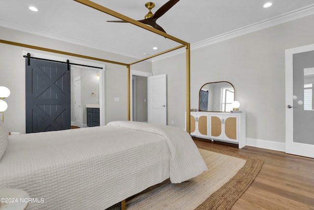 bedroom with ornamental molding, hardwood / wood-style floors, a barn door, ensuite bathroom, and ceiling fan