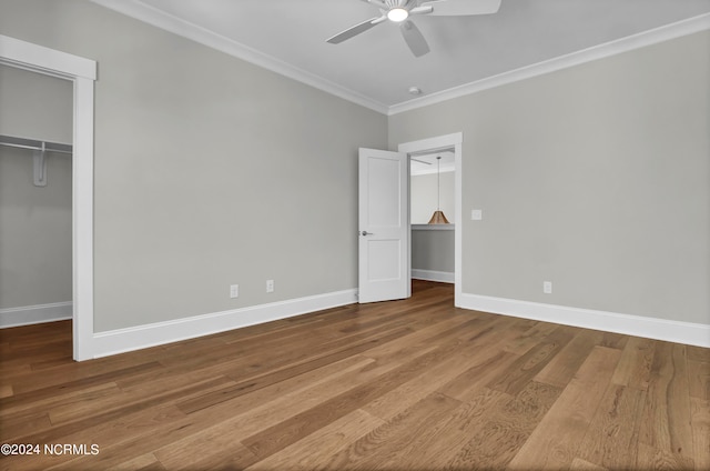 unfurnished bedroom featuring a closet, wood-type flooring, a spacious closet, ornamental molding, and ceiling fan