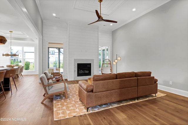 living room with crown molding, a large fireplace, wood-type flooring, and ceiling fan with notable chandelier