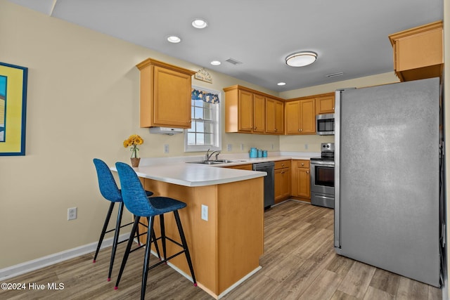 kitchen with appliances with stainless steel finishes, sink, light wood-type flooring, kitchen peninsula, and a kitchen breakfast bar