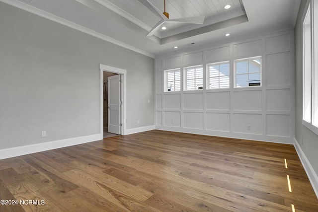 empty room with hardwood / wood-style floors, ceiling fan, plenty of natural light, and a raised ceiling