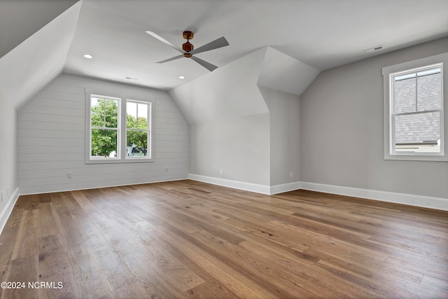 additional living space with ceiling fan, lofted ceiling, light wood-type flooring, and wooden walls