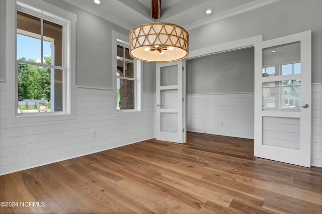 unfurnished dining area with crown molding, wood-type flooring, a healthy amount of sunlight, and wooden walls