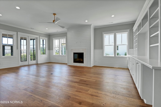 unfurnished living room featuring ceiling fan, a large fireplace, crown molding, and hardwood / wood-style floors