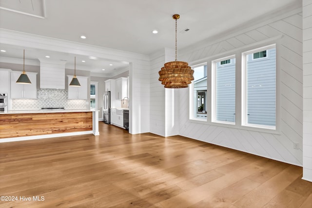 unfurnished living room featuring ornamental molding, hardwood / wood-style floors, wooden walls, and sink