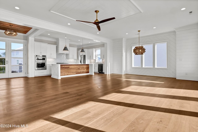 unfurnished living room with wooden walls, ceiling fan with notable chandelier, and light hardwood / wood-style floors