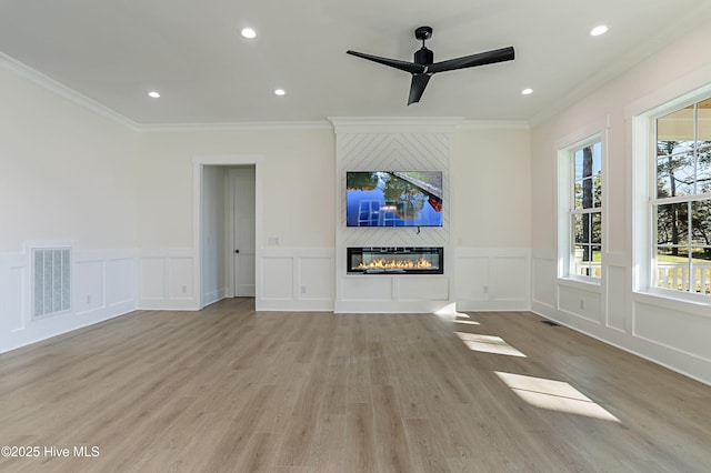 unfurnished living room with a ceiling fan, visible vents, ornamental molding, and a decorative wall