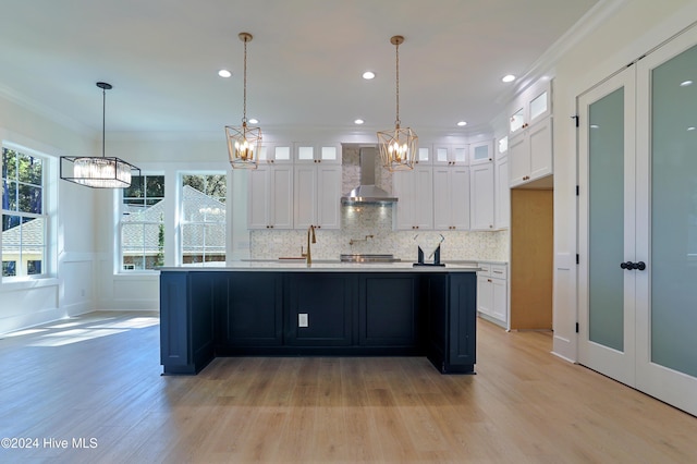 kitchen with light wood-style floors, white cabinetry, light countertops, wall chimney exhaust hood, and a notable chandelier