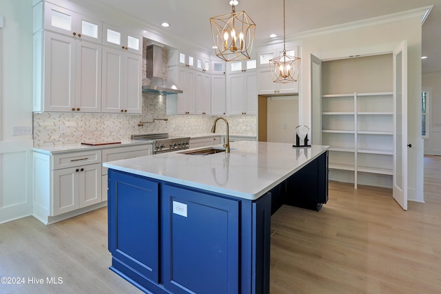 kitchen featuring light wood-type flooring, white cabinets, a sink, and wall chimney range hood