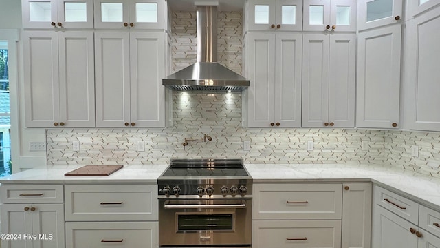 kitchen with white cabinets, stainless steel range, backsplash, and wall chimney range hood