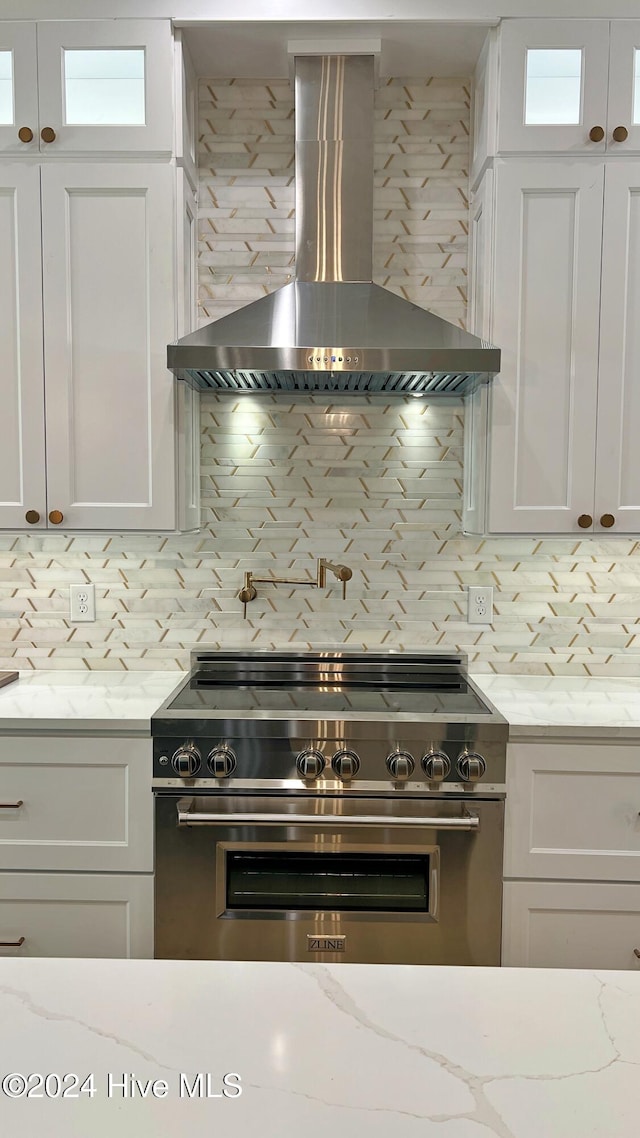 kitchen with wall chimney exhaust hood, high end stainless steel range oven, tasteful backsplash, and white cabinetry