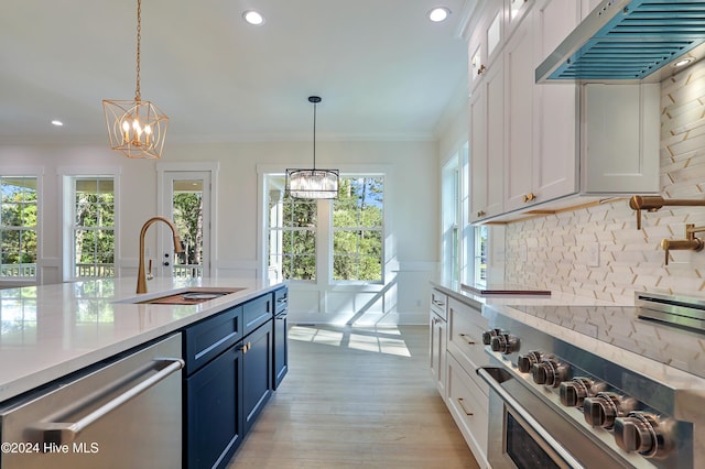 kitchen with a sink, blue cabinets, an inviting chandelier, exhaust hood, and appliances with stainless steel finishes